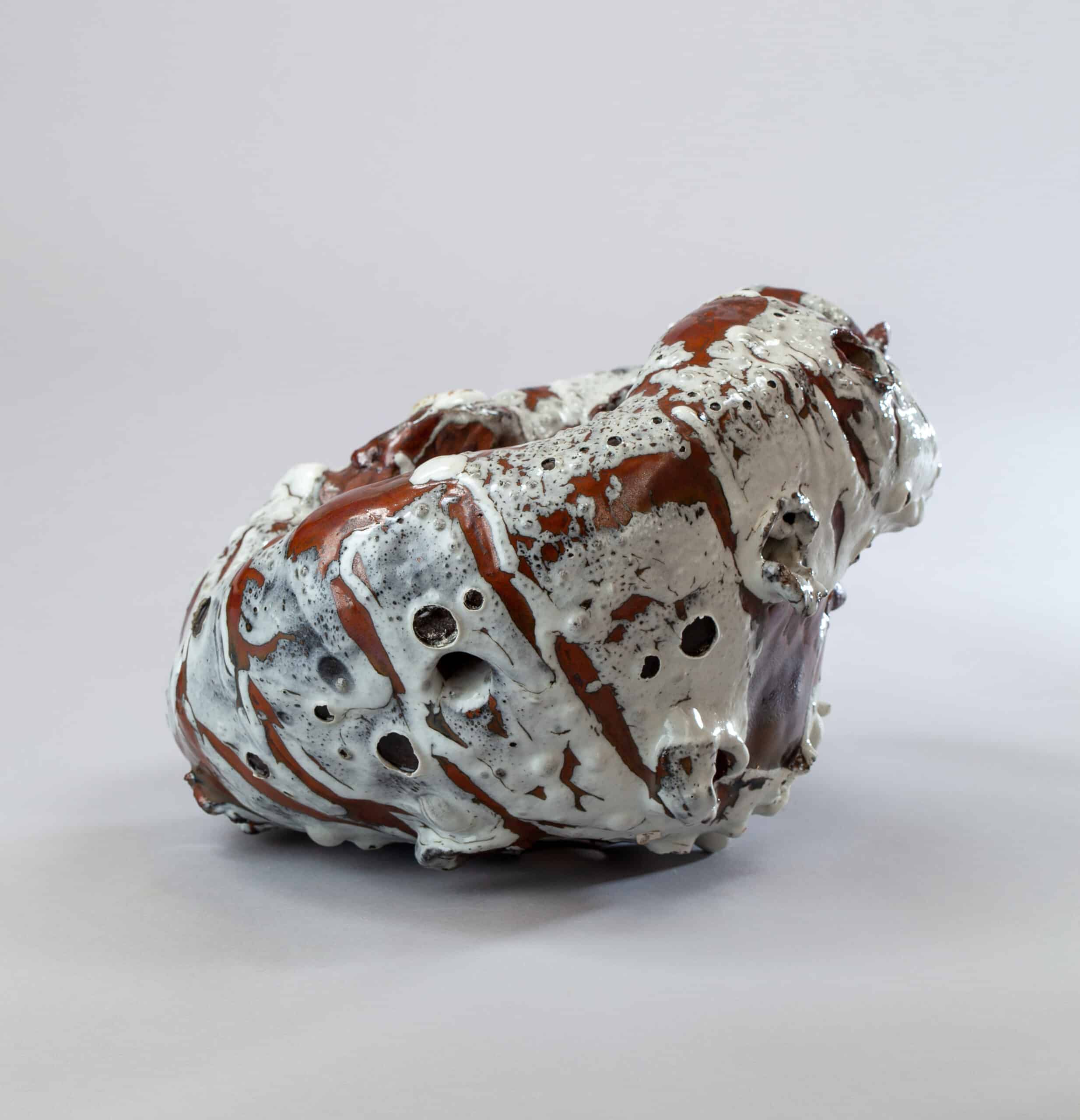 Sculpture céramique abstraite aux émaux blancs coulés et bruns rougeâtres, présentant des textures bullées et des trous.