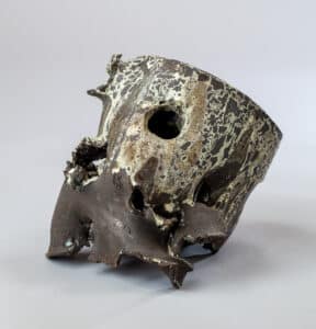 Sculpture céramique abstraite, brute et sombre, avec glaçure craquelée blanc-vert et une grande ouverture centrale.