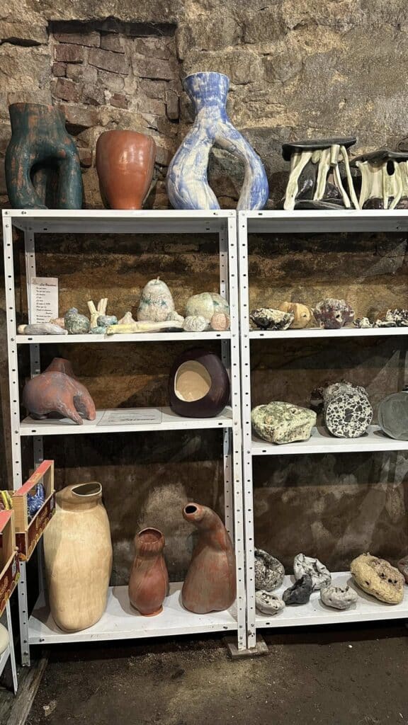 Vases Céramiques Organiques et Sculptures d'Art Sculptures céramiques organiques et vases texturés, bleu et terre cuite, exposés sur des étagères métalliques devant un mur de pierre brute.