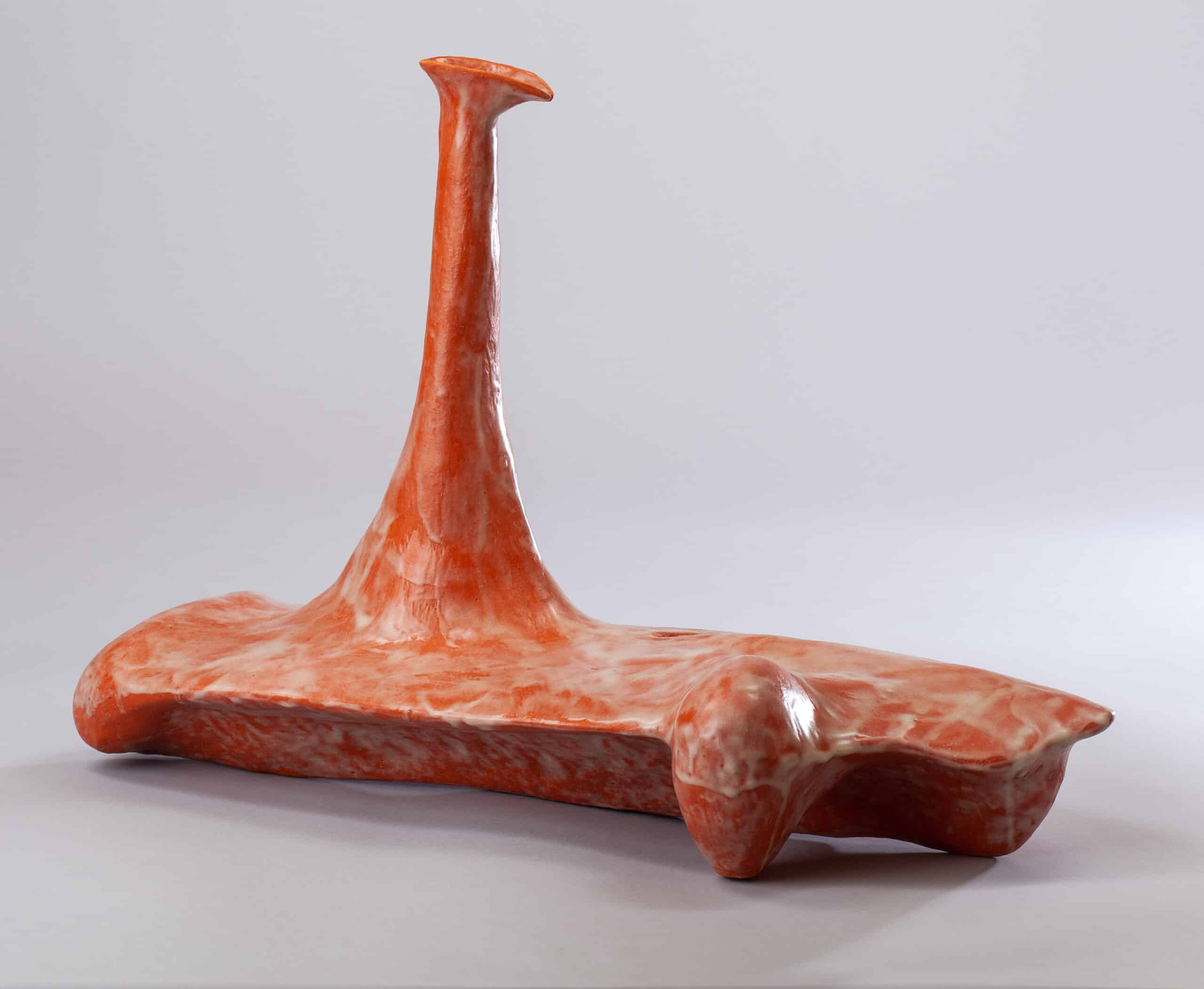Sculpture abstraite en céramique rouge-orangé brillant avec un col étroit et évasé sur une base allongée, sur fond gris clair.