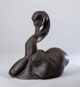 Sculpture en céramique sombre texturée, brun foncé, représentant un cygne au cou fortement courbé et au corps arrondi.