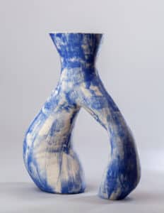 Vase sculptural en céramique blanche et bleu cobalt, présentant une forme en sablier avec une ouverture centrale audacieuse et une texture brossée.