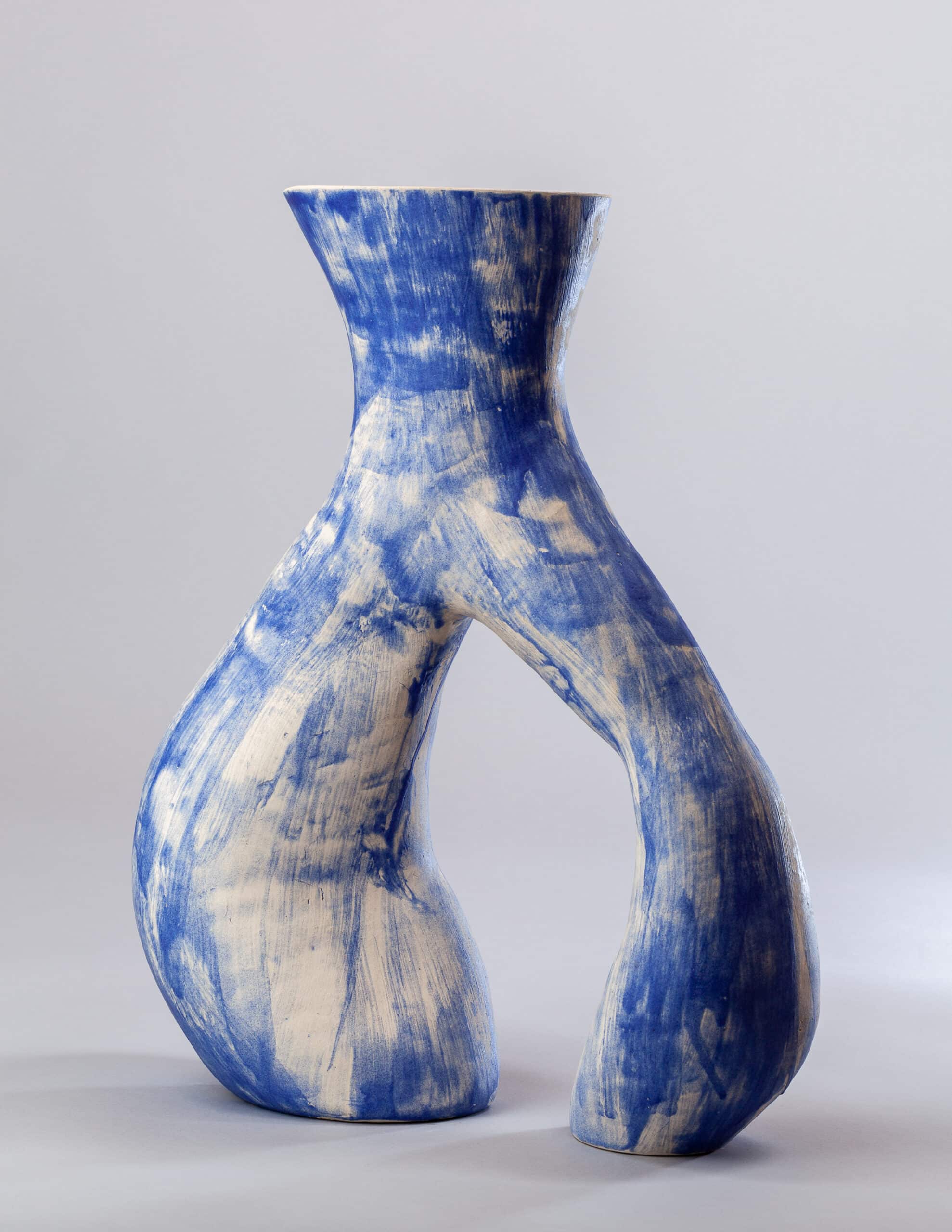 Vase sculptural en céramique blanche et bleu cobalt, présentant une forme en sablier avec une ouverture centrale audacieuse et une texture brossée.