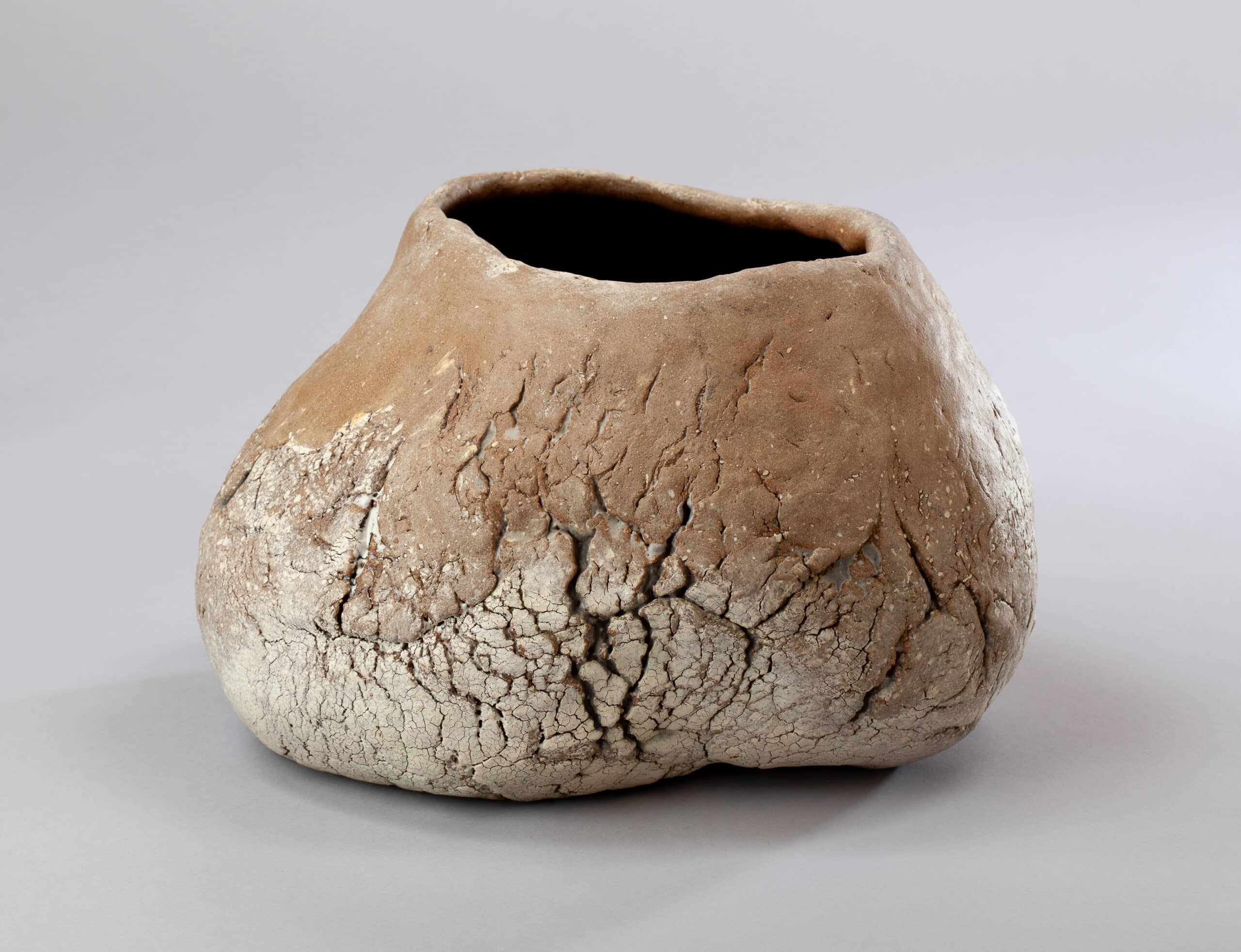 Vase en céramique texturée terre cuite, à la forme organique et irrégulière, avec un col sombre et une base craquelée blanche.