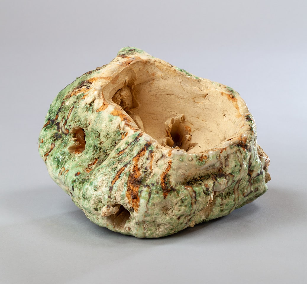 Sculpture en céramique organique verte et beige à texture brute émaillée, évoquant une forme rocheuse rustique.
